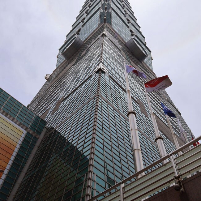 Towering glass-clad skyscraper photographed from ground level, with flagpoles in the foreground.